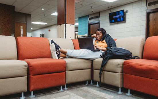 Photo of a student lounging on her laptop in the commons