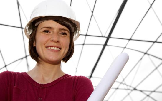 A person in a red sweater and white hard hat holds rolled-up papers